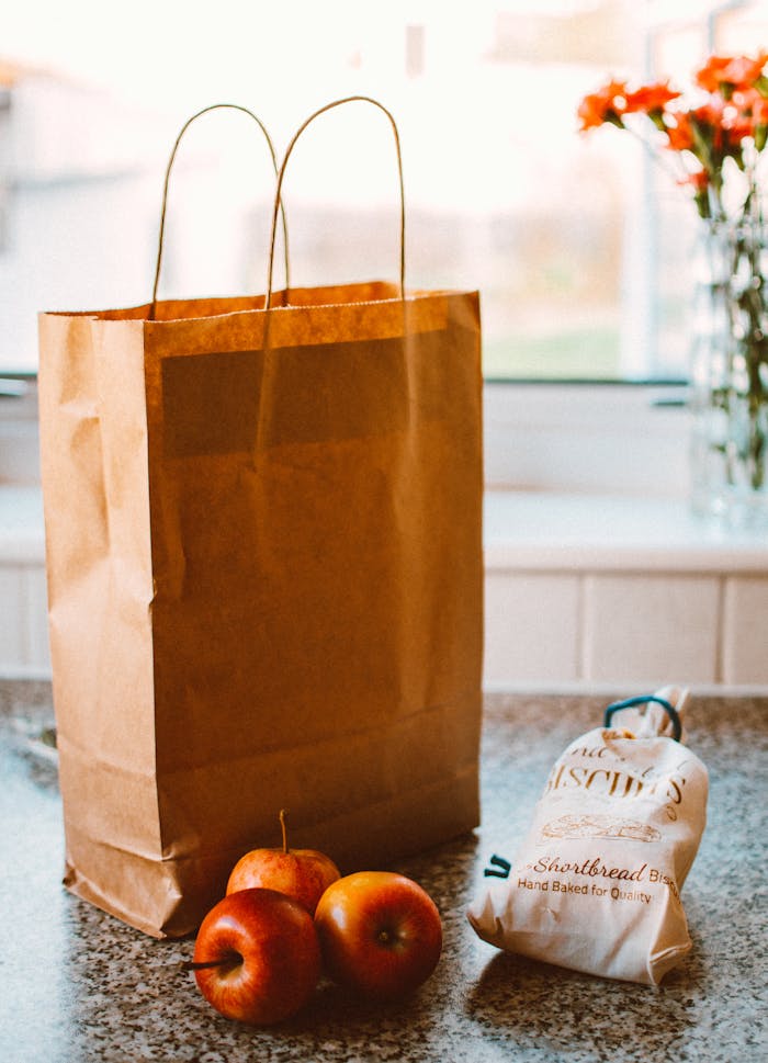 A paper bag with apples and packaged goods on a kitchen countertop, lit by natural light.