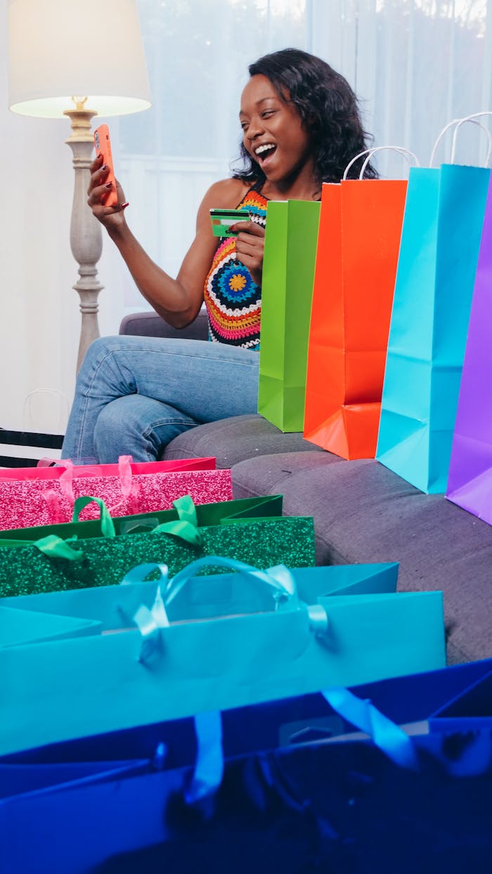 About A woman enjoys online shopping with a smartphone, surrounded by colorful shopping bags indoors.